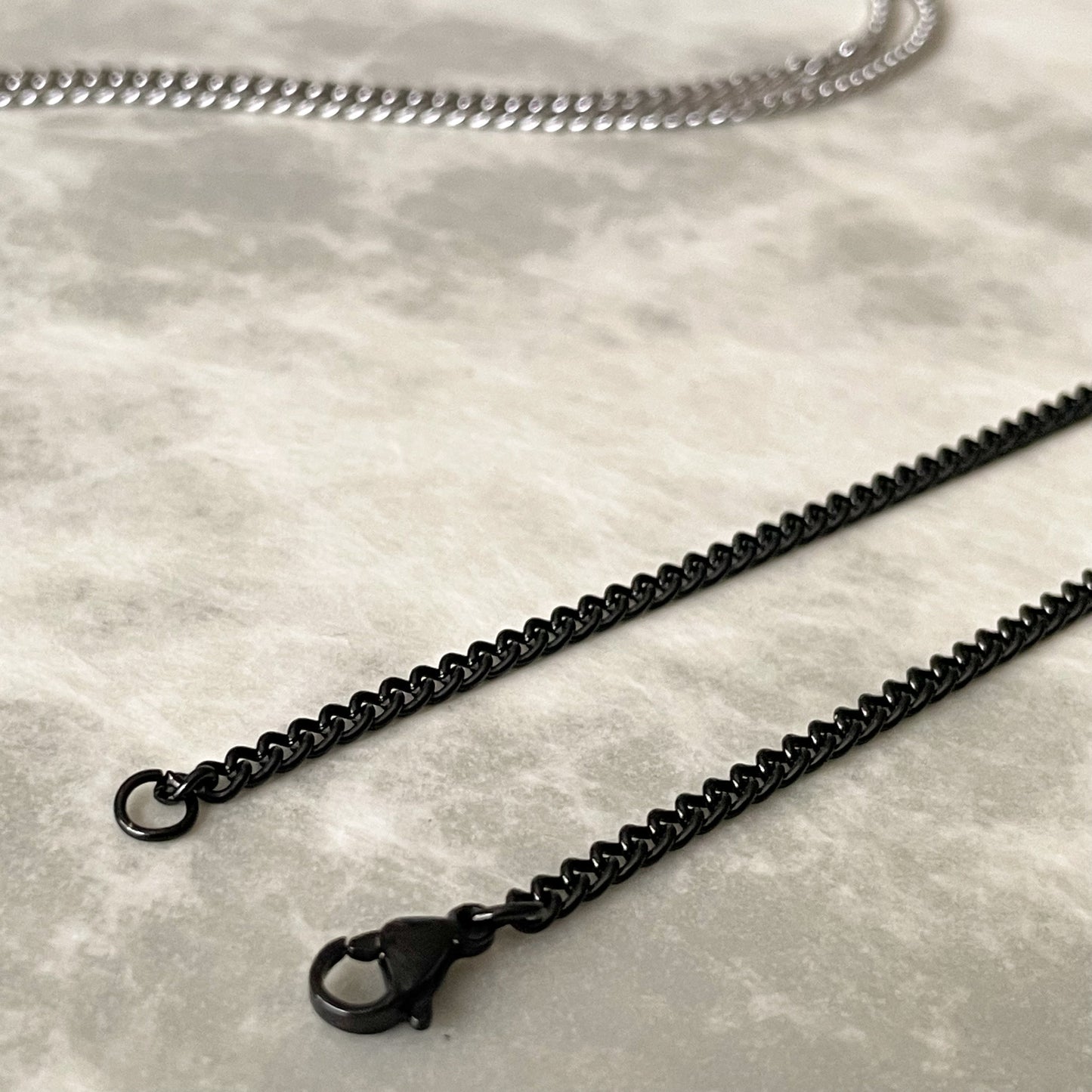 Close up view of the black curb chain's lobster claw clasp on a textured gray surface