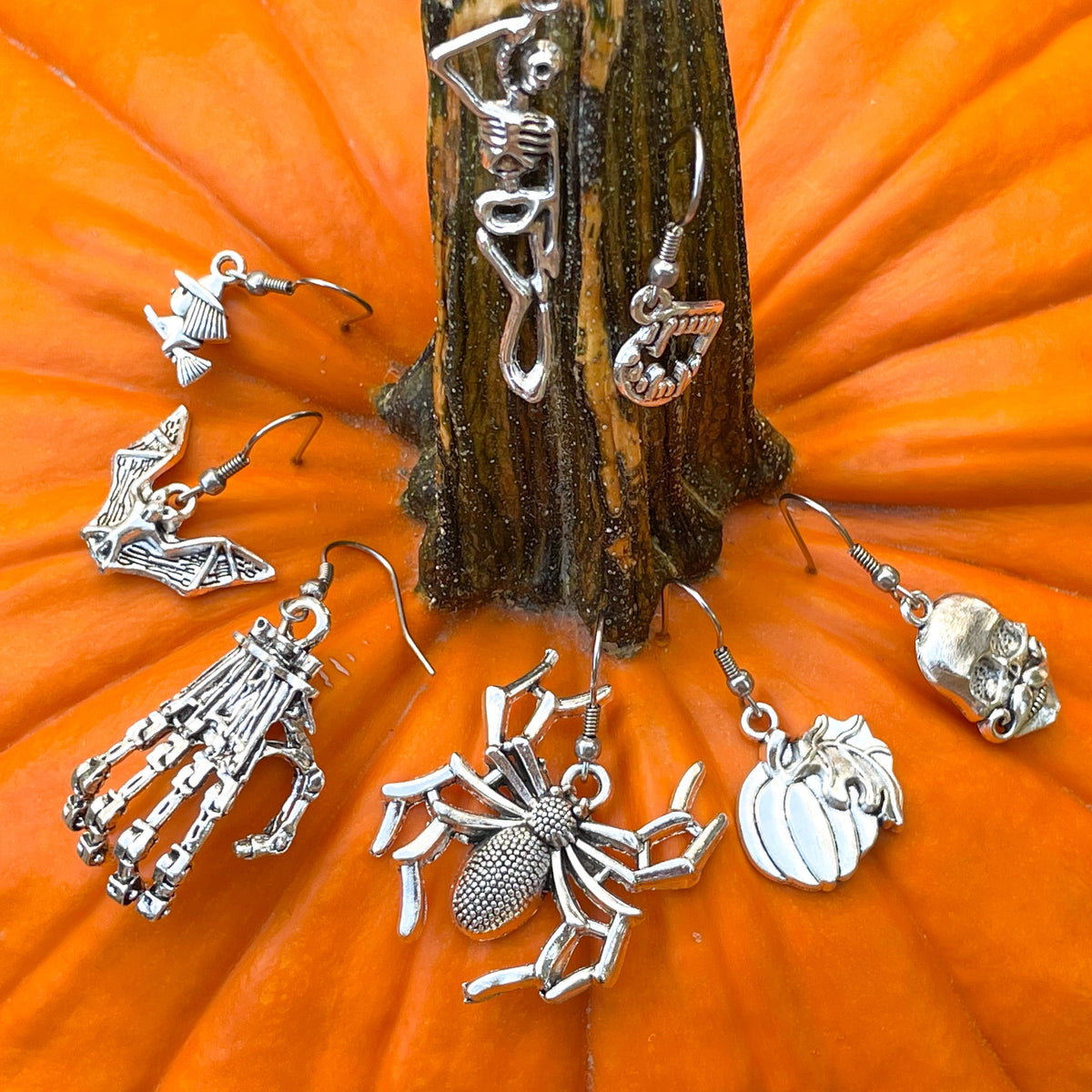 Silver Halloween-themed earrings on an orange pumpkin background