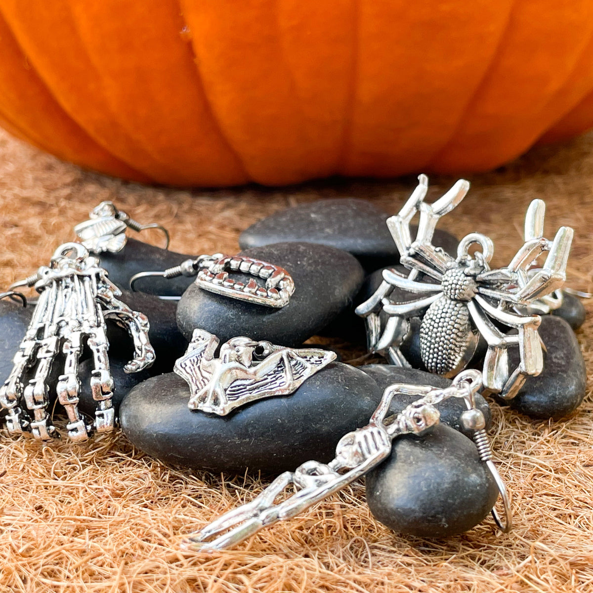Silver Halloween-themed dangle earrings on black stones with a pumpkin in the background