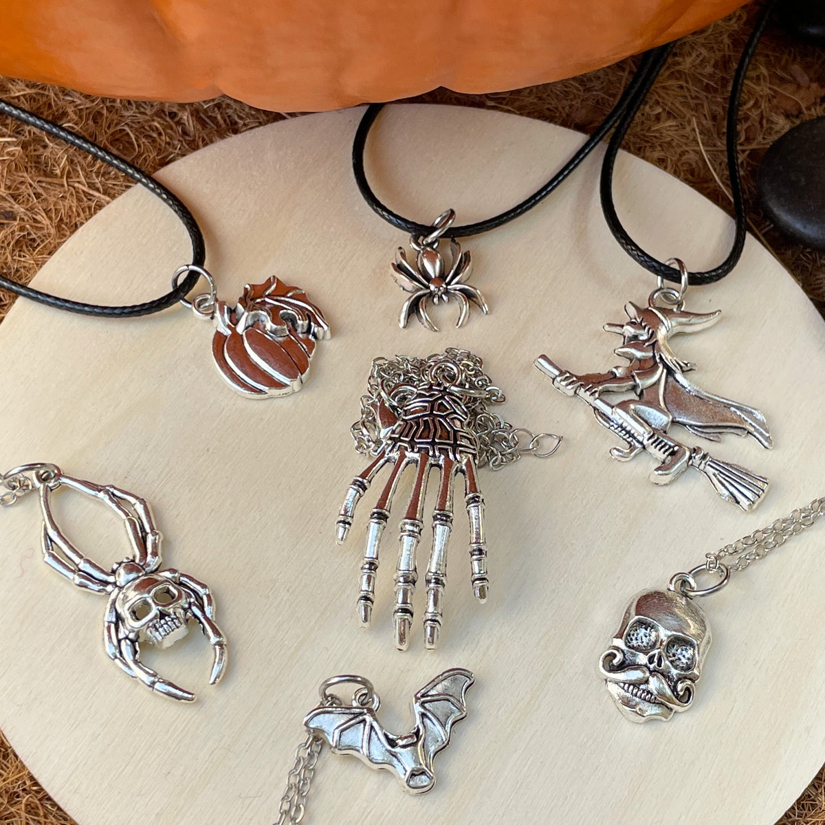 Collection of silver Halloween-themed pendants on a white plate with a pumpkin and stones in the background.