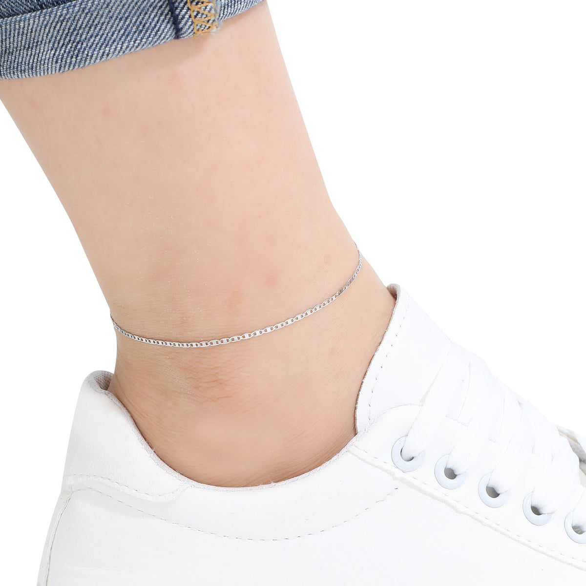Silver anklet on a person's ankle with a white sneaker and denim jeans in the background