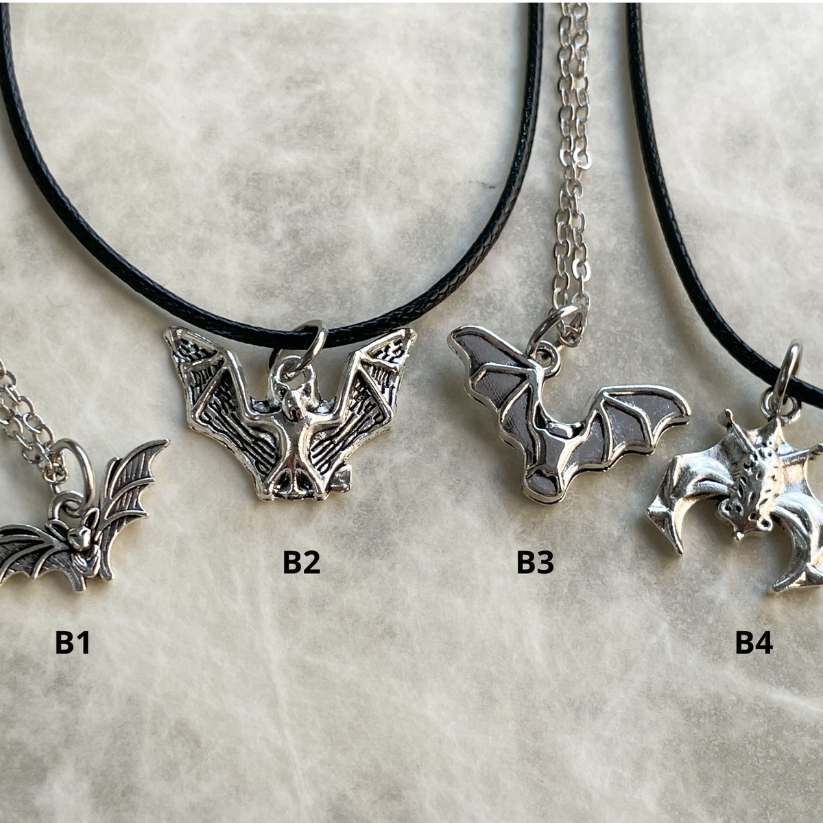 Four silver bat-shaped pendants on black cords against a light gray background.