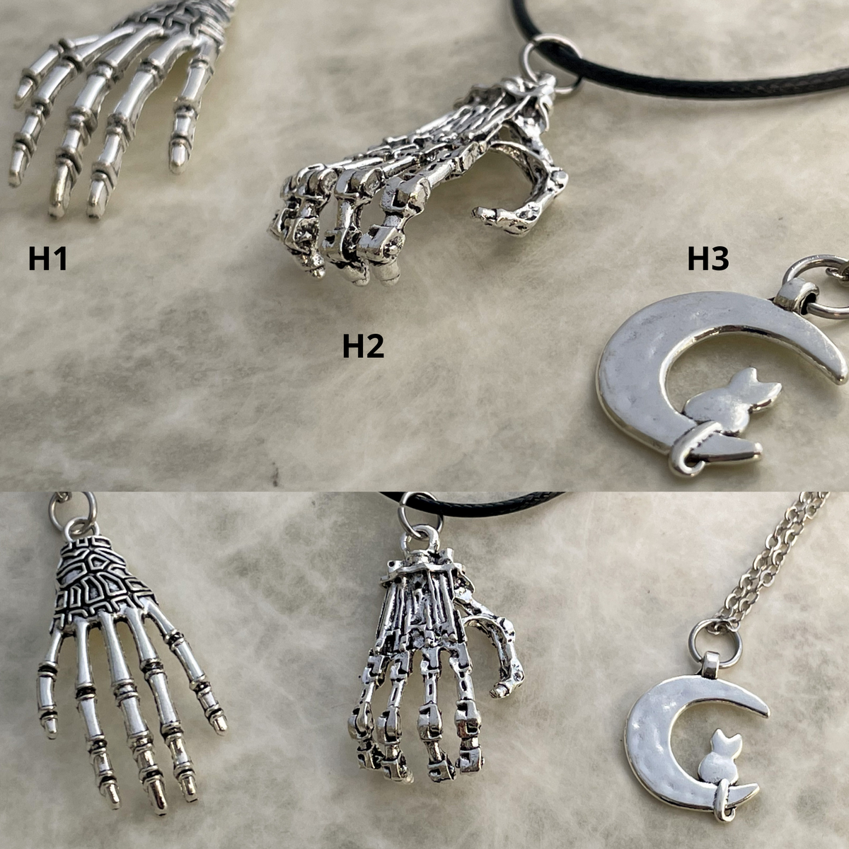 Collection of silver pendants including a skeleton hand, crescent moon with a cat, and other designs on a textured surface.