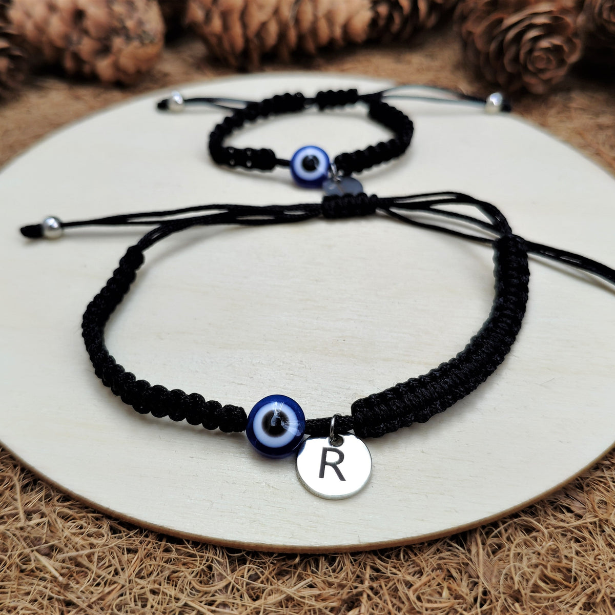 Black macrame bracelets with evil eye charms and silver initials on a white plate.