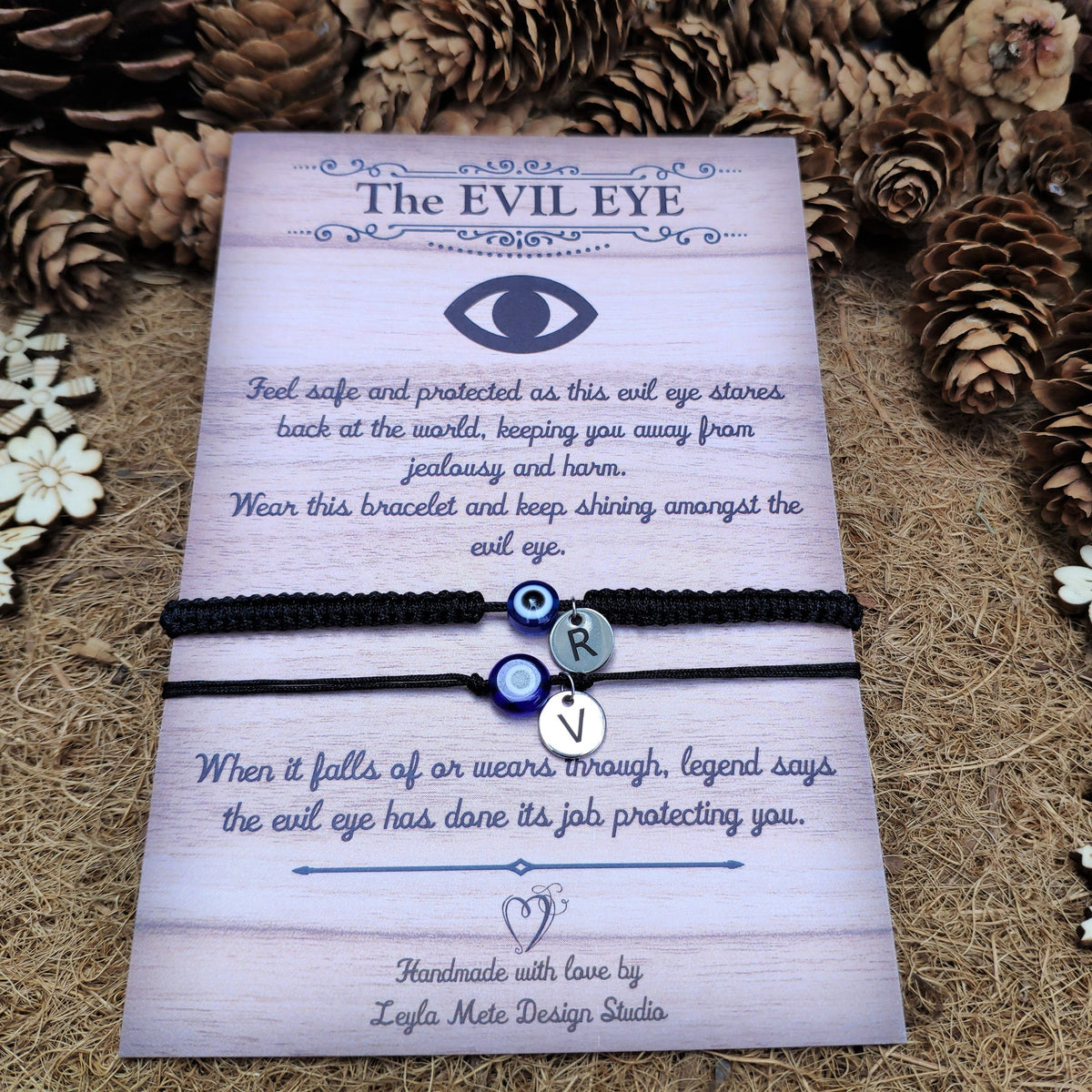 Bracelet with 'The Evil Eye' design on a decorative card surrounded by pinecones and flowers.