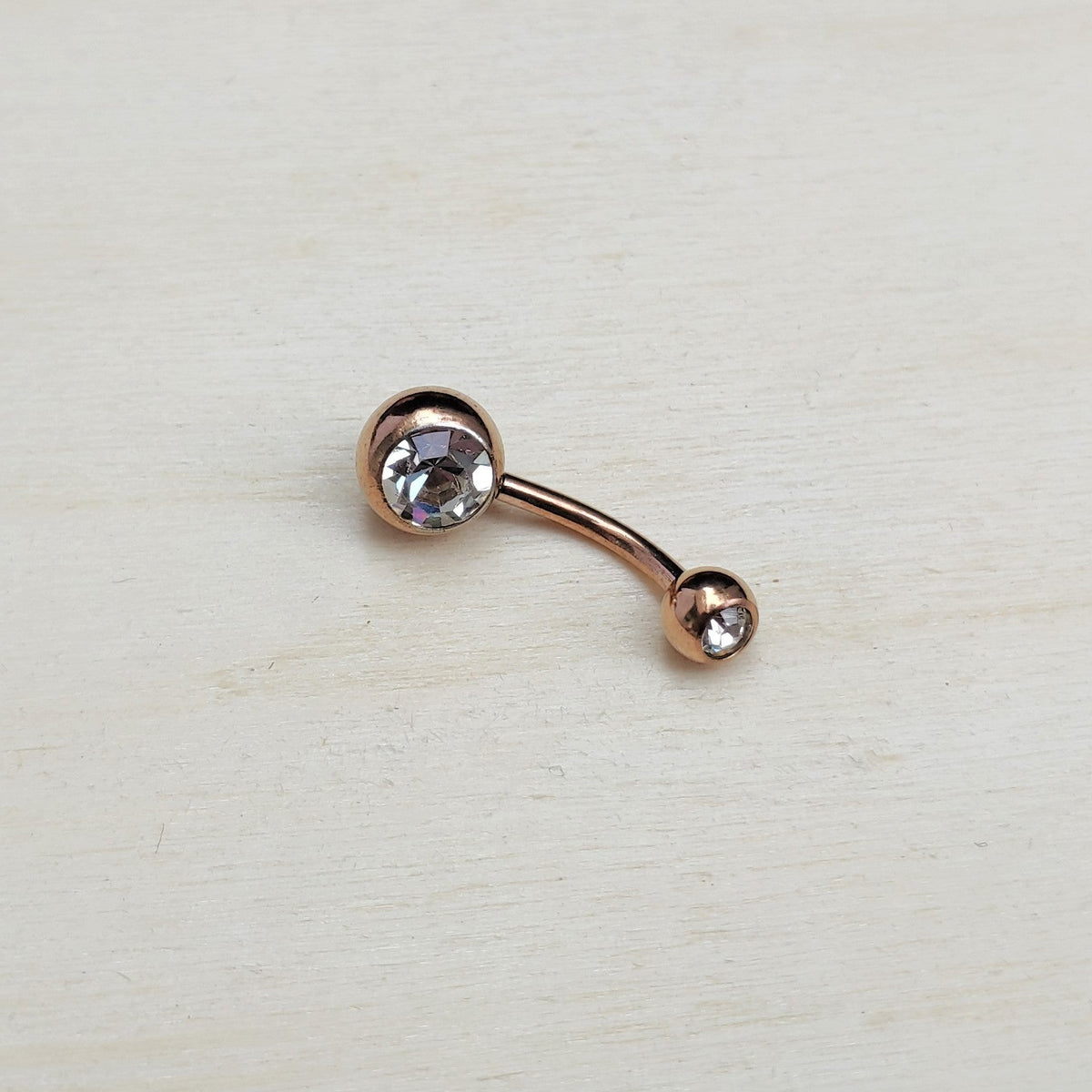 Rose gold belly button ring with a clear gemstone on a light beige background