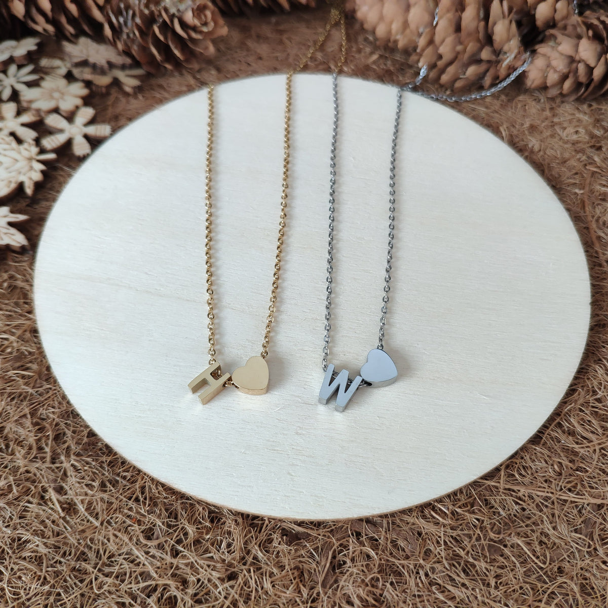 Two necklaces, one with heart and 'H' and one with heart and 'W' on a white wooden plate