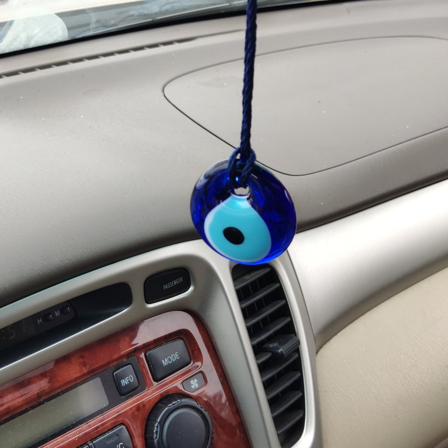 Blue glass evil eye talisman hanging from a car's rearview mirror.
