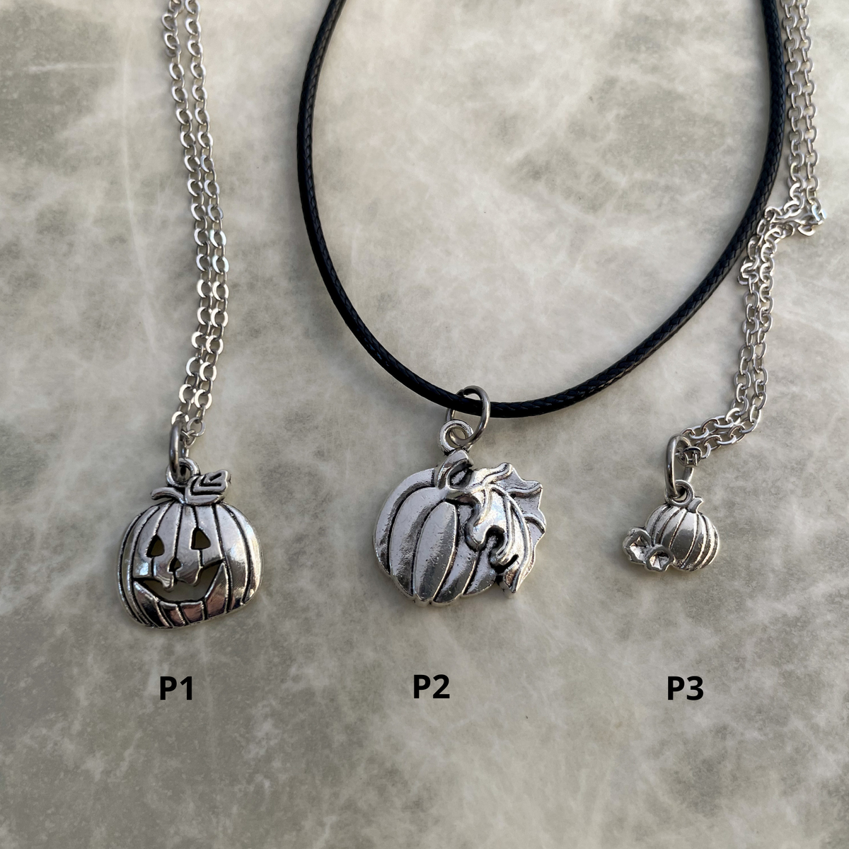 Three silver pumpkin charm necklaces on a gray stone surface