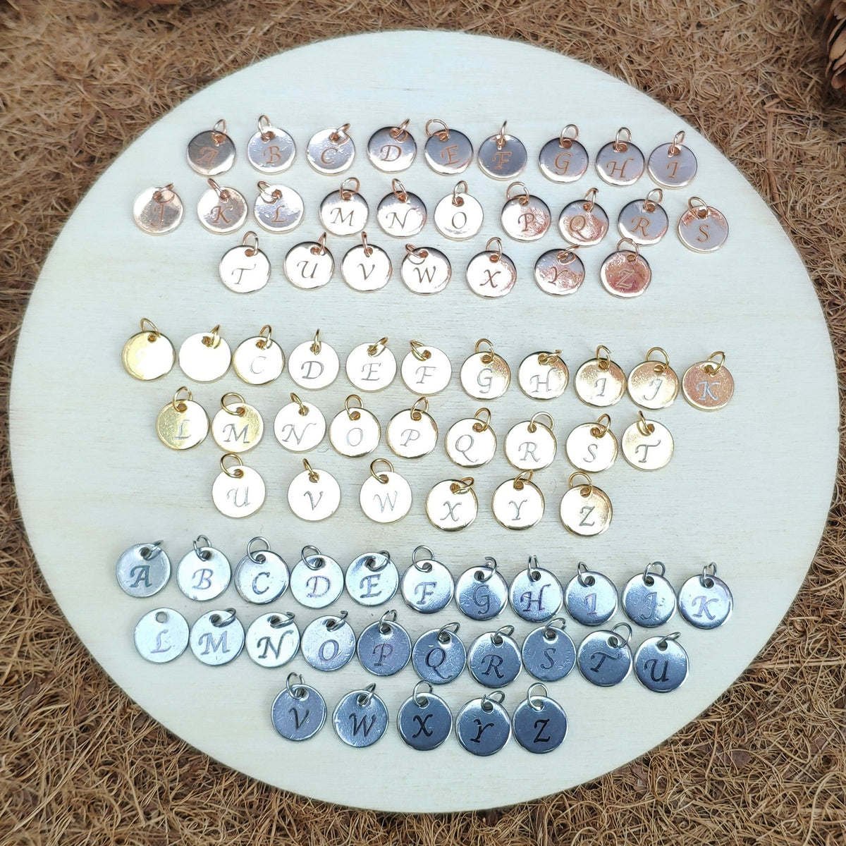 Alphabet charms on small discs in gold, silver and rose gold on a round white board