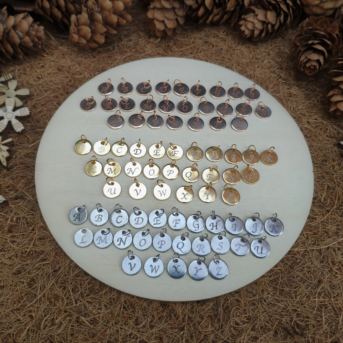 Round white board with alphabet charms surrounded by pine cones and snowflakes on a textured brown background