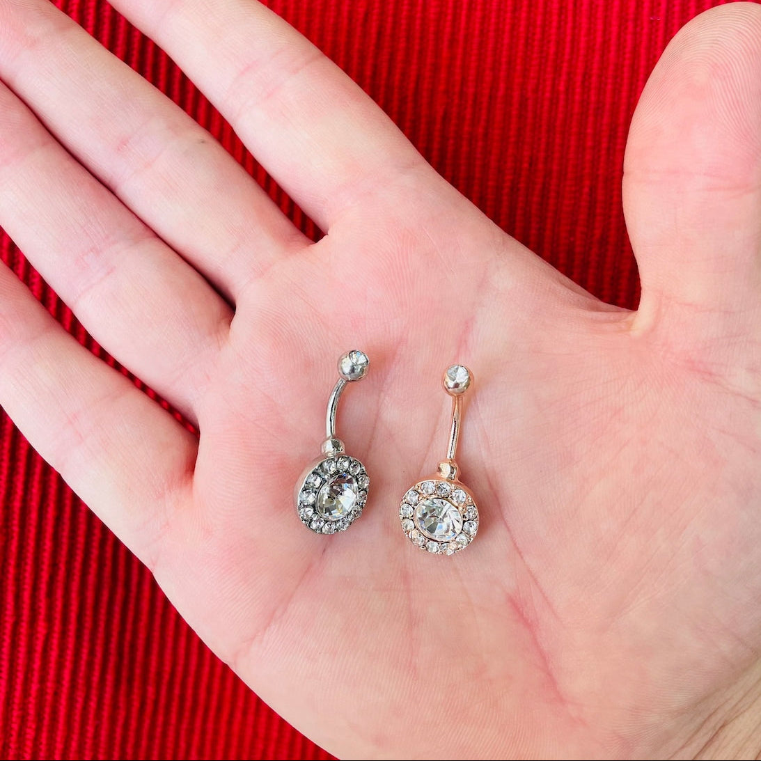 Two belly button rings on a hand with a red background