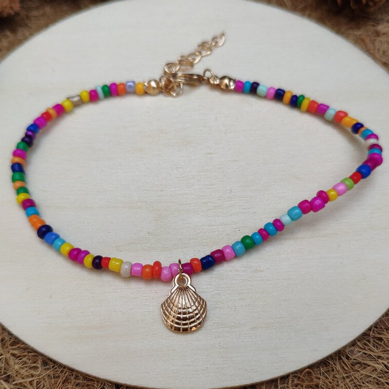 Colorful beaded ankle bracelet with a gold shell charm and gold clasp on a white surface