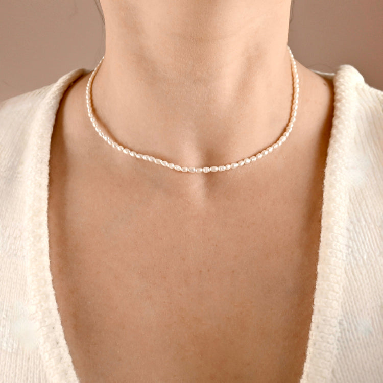 Delicate natural pearl necklace worn by a person with a neutral background