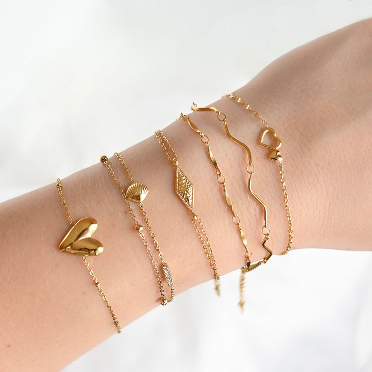 Stylish wrist stack: Model in dark pink sweater wearing a variety of cuff bracelets from lower arm to wrist, including Chunky Twisted, Tunnel, Cube and Ball, Molten, and Braided styles. Top view.