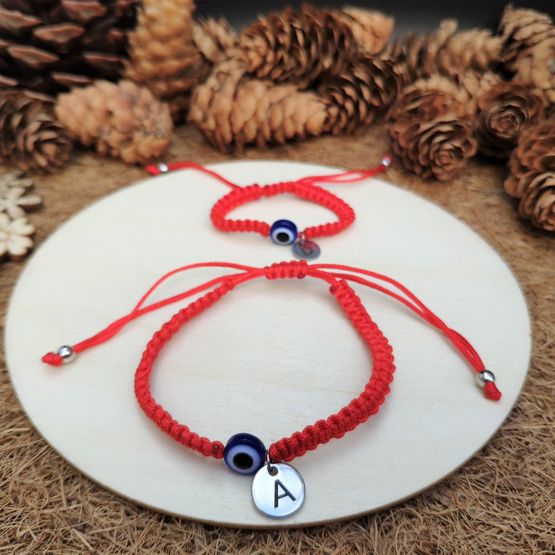 Red braided bracelet with an 'A' charm on a white plate surrounded by pine cones and snowflakes.