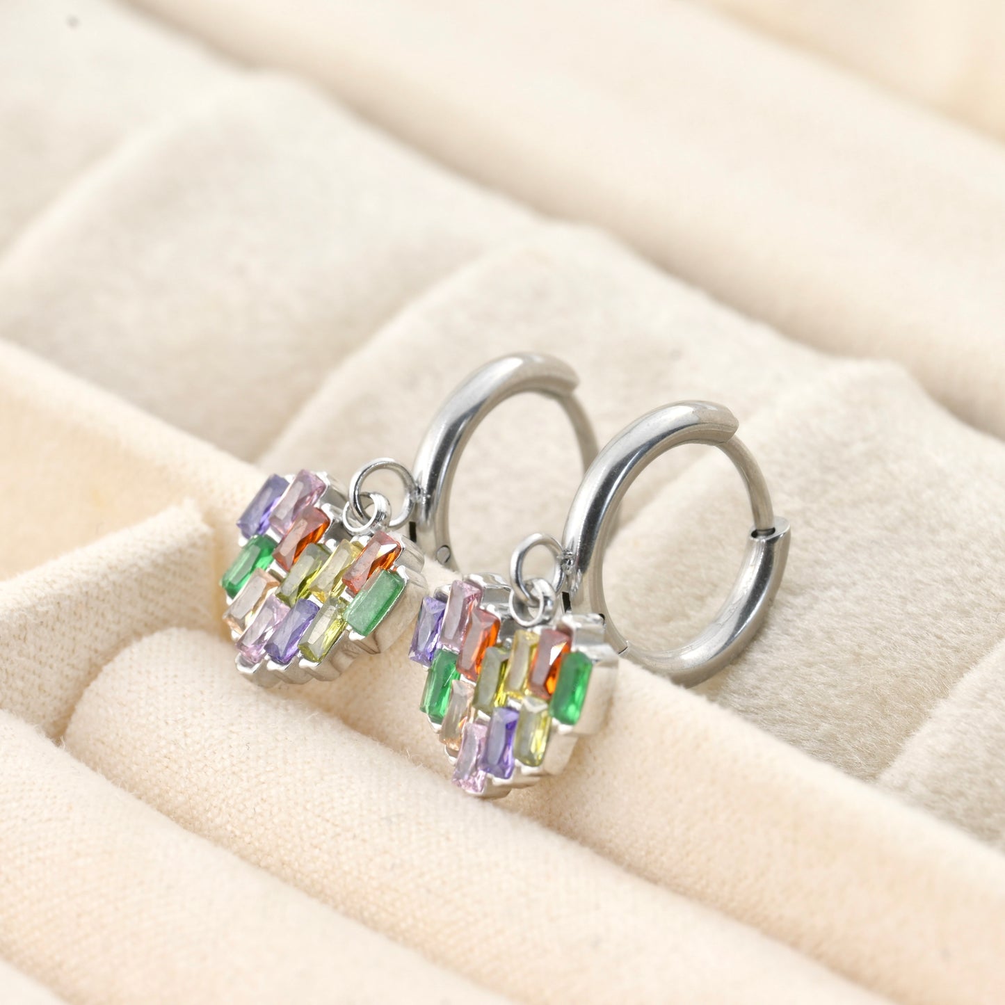 Silver hoop earrings with heart charm on a beige cushion