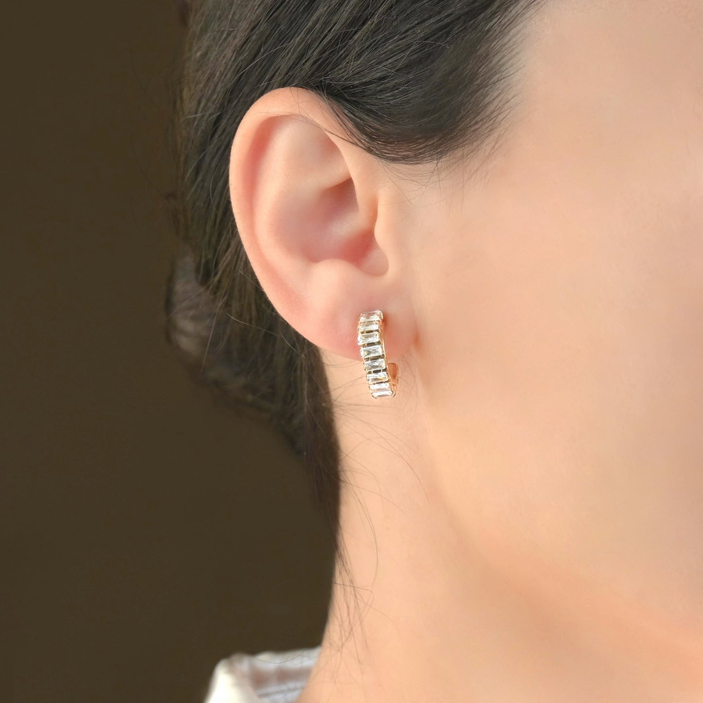 Close-up of an ear wearing gold baguette hoop earrings with a blurred background