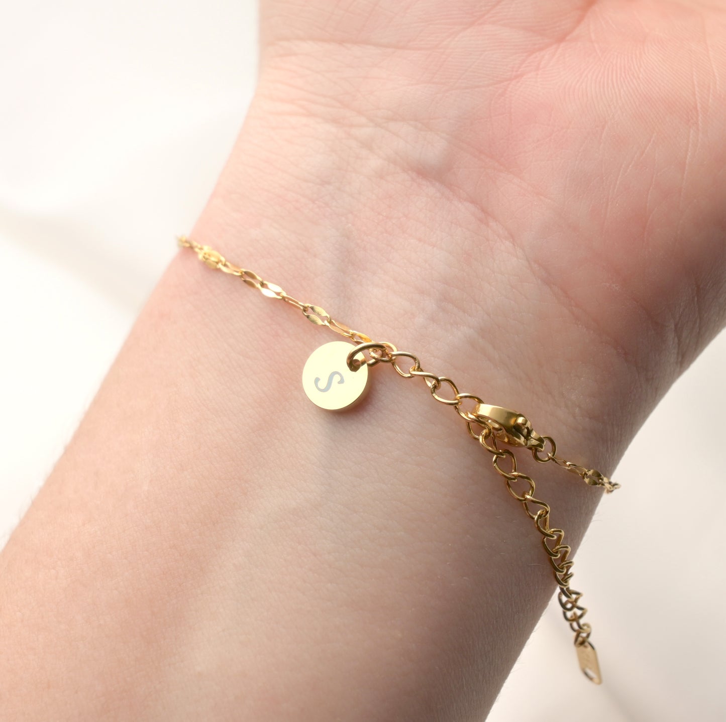Gold mariner bracelet with a small engraved round charm ewith 'S' on a wrist against a neutral background