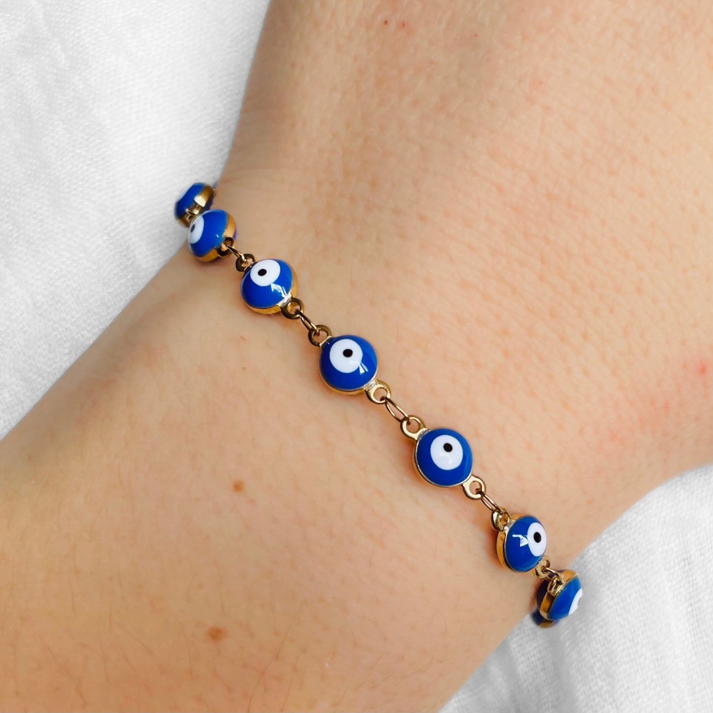Gold Bracelet with blue round evil eye beads on a wrist against a white background