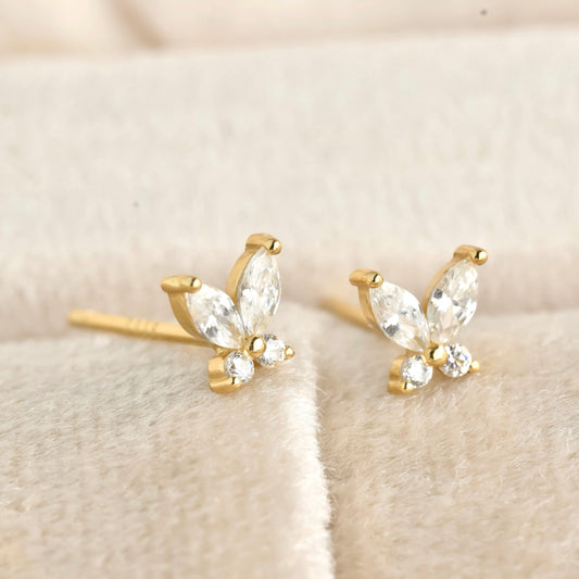 Gold butterfly-shaped earrings with clear gemstones on a soft beige background
