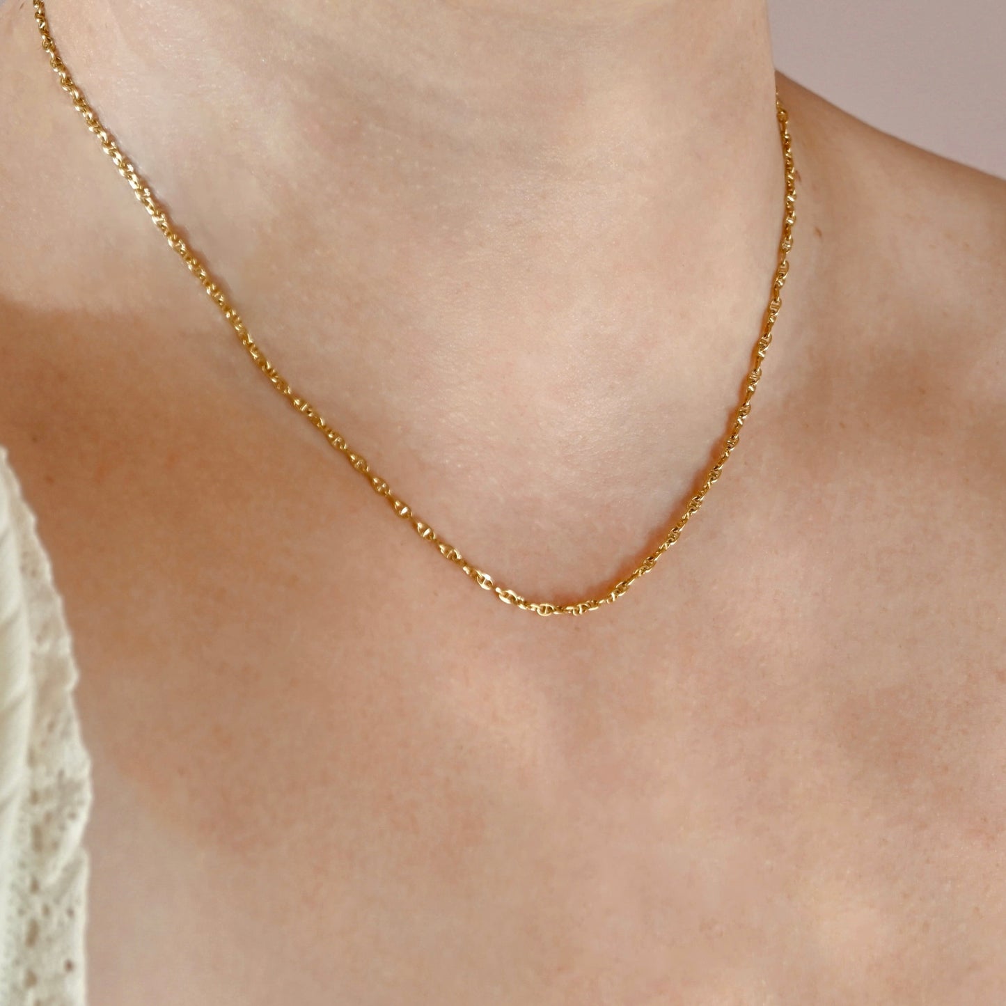A close-up of a delicate gold chain necklace worn on a person's neck and upper chest, with a light-colored lace top partially visible on the left.