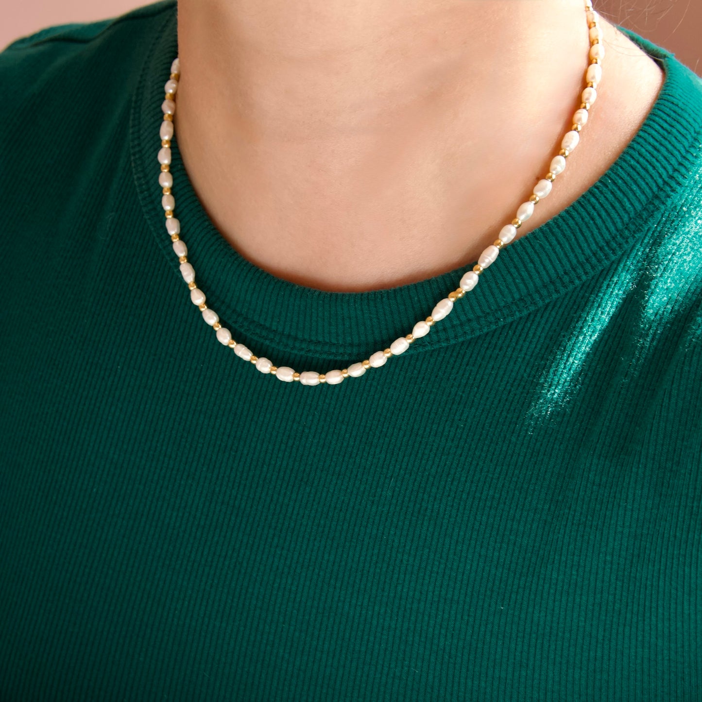 A close-up of a person wearing a single-strand baroque pearl necklace over a dark green ribbed knit top.