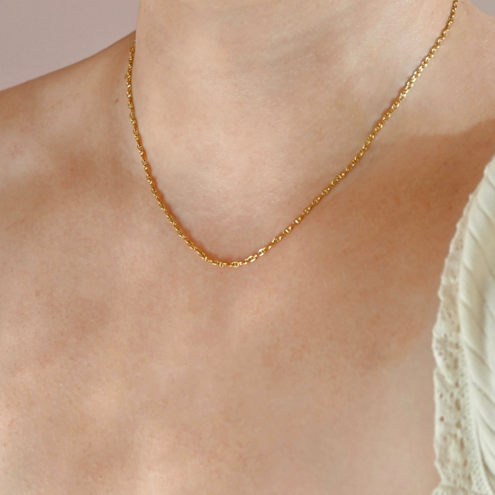 A close-up of a delicate gold chain necklace worn on a person's neck and upper chest, with a white lace-trim top visible on the right side.