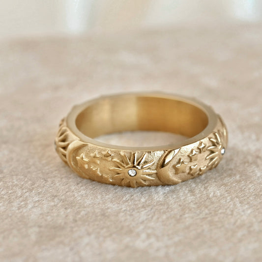 Thick gold ring with embossed sun with CZ centerpiece, moon and stars  on a beige surface
