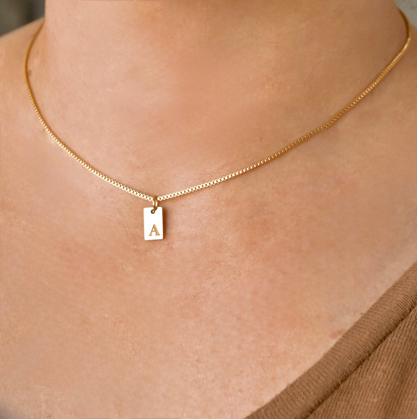 Gold  box chain necklace with a rectangle pendant featuring the letter 'A' on a person's neck.