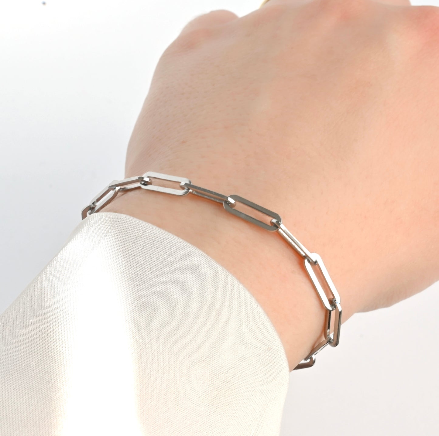 Silver paperclip bracelet on a wrist with a plain background
