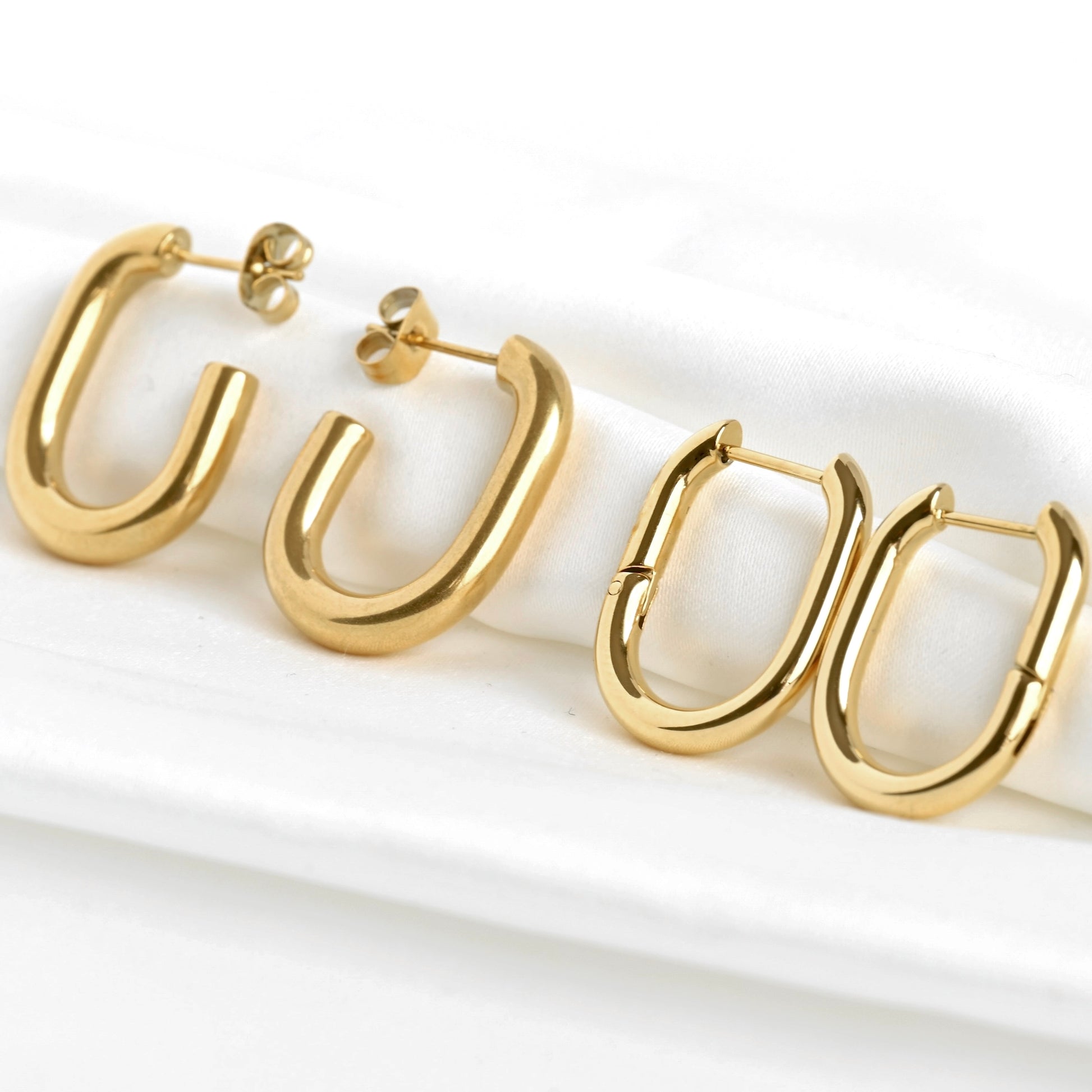 Pair of gold paperclip hoop earrings, one bold and thick with push-back closure, one thinner with cloicker closure on a white background