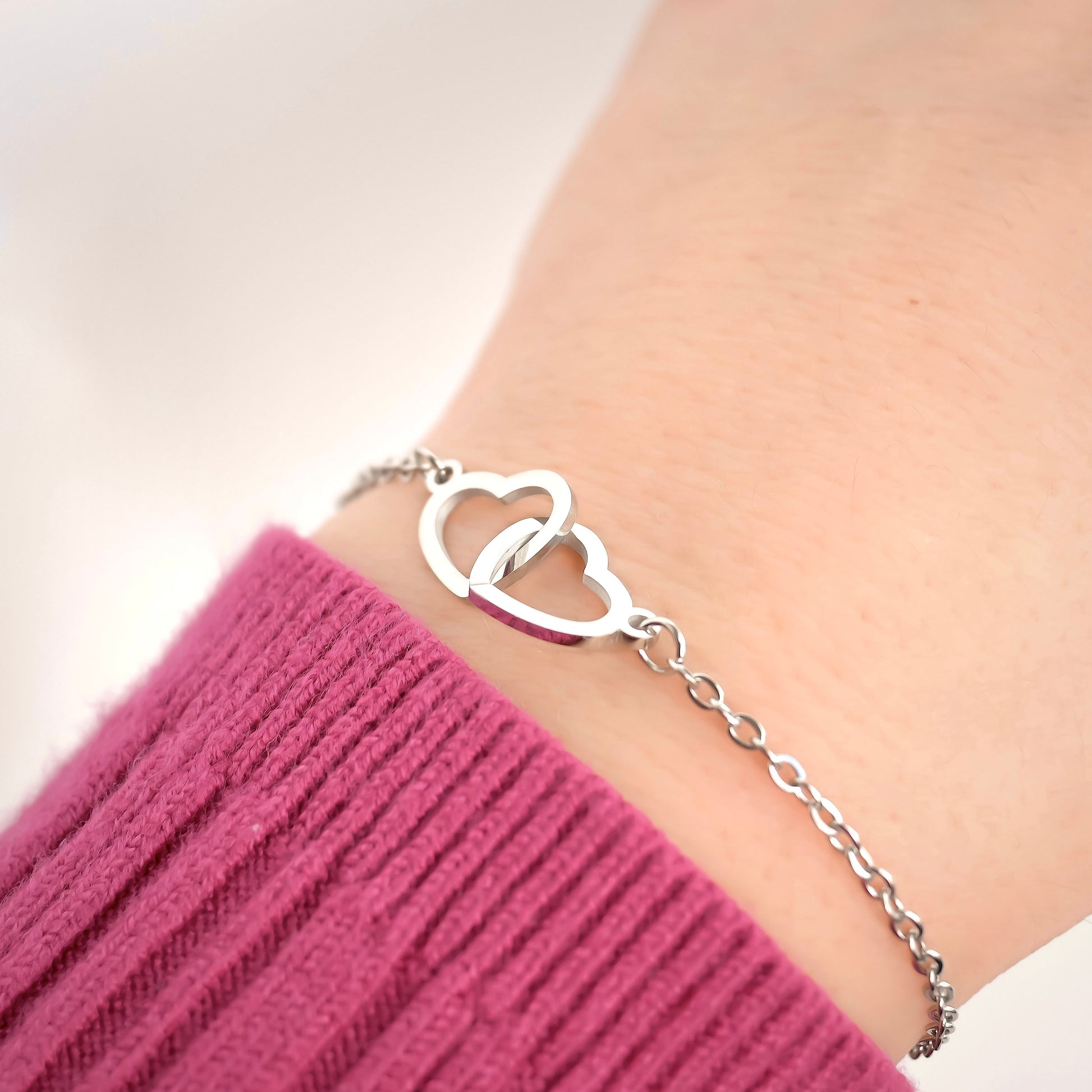 Silver bracelet with heart design on a wrist wearing a pink sleeve.