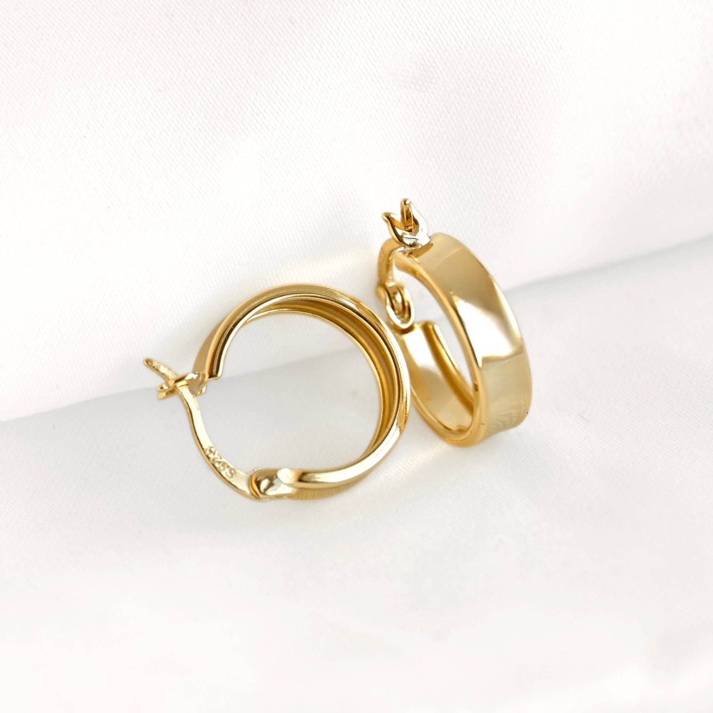 A pair of small polished yellow gold hoop earrings displayed on a clean white fabric background.