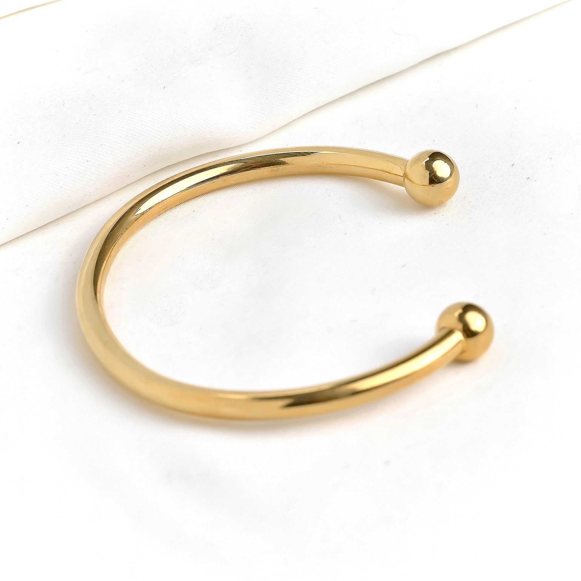 Gold cuff bracelet with ball ends on a white background