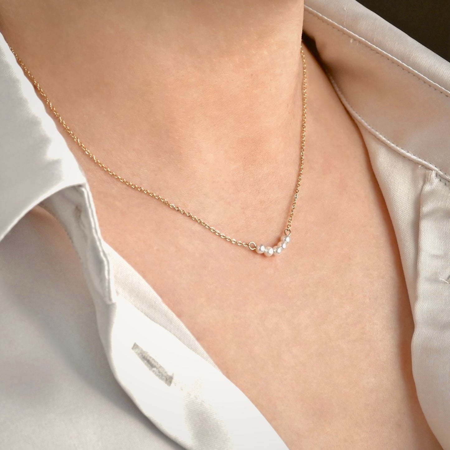 Gold  curved bar pearl necklace worn by a person in a white shirt.