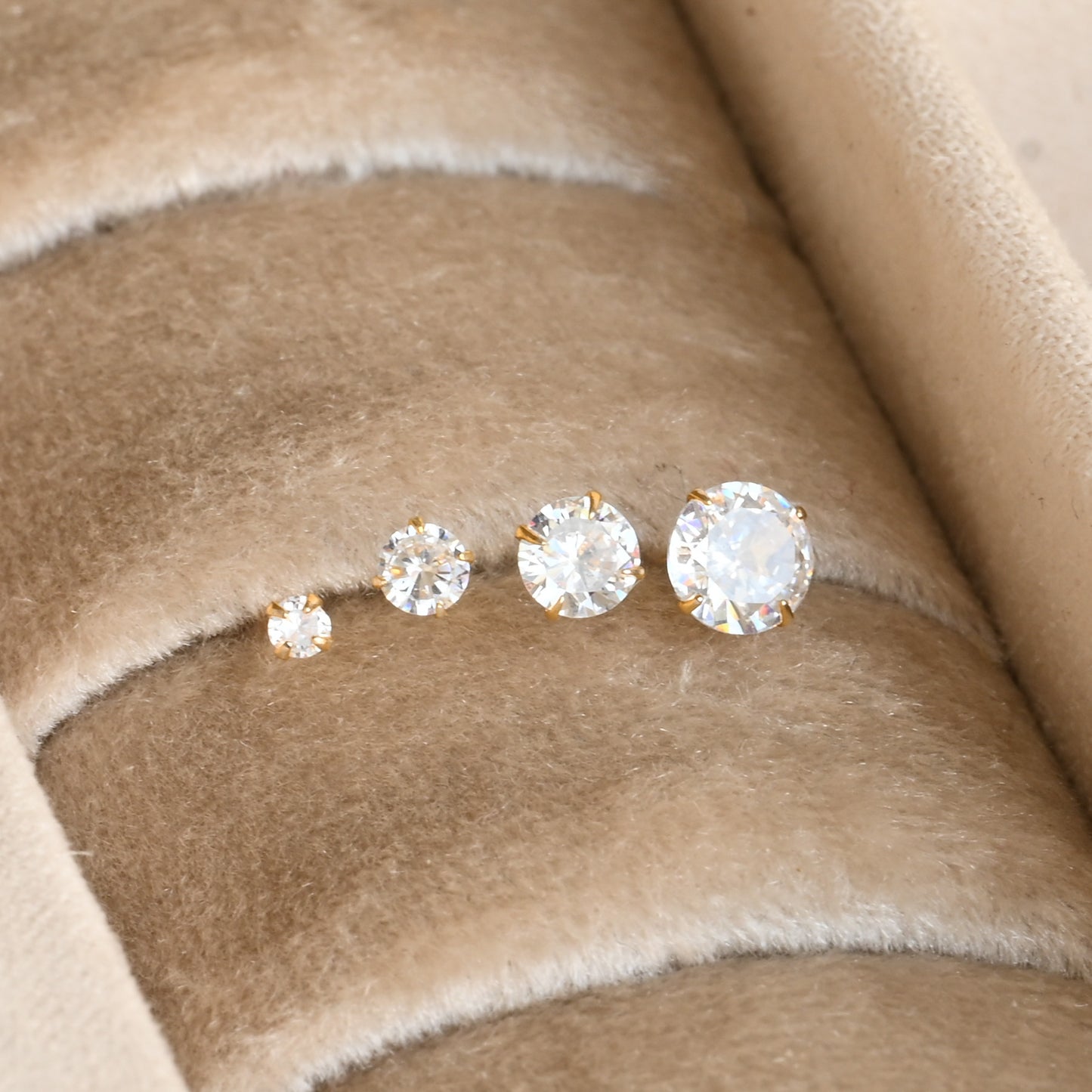 diamond stud earrings in four sizes on a beige fabric background