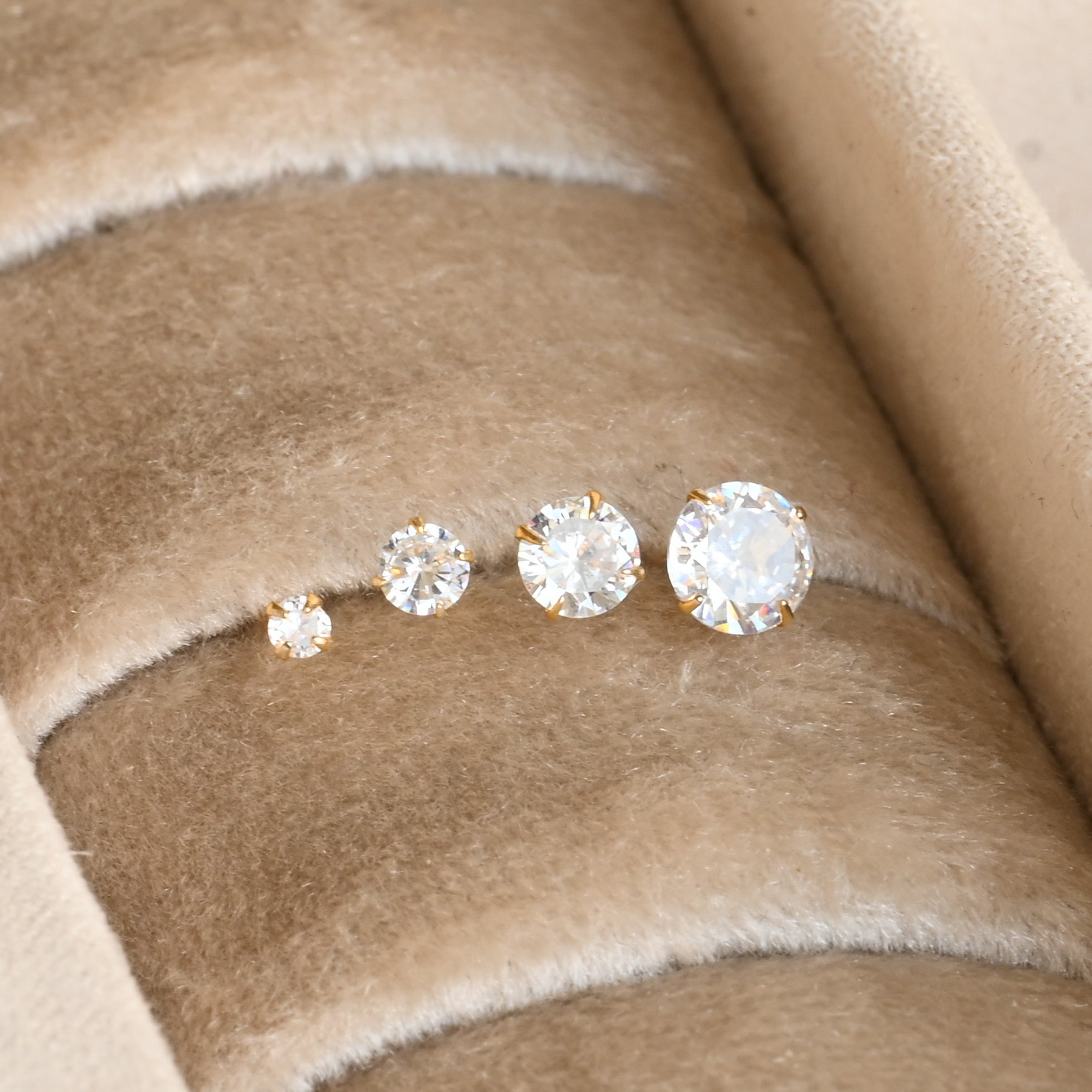 diamond stud earrings in four sizes on a beige fabric background