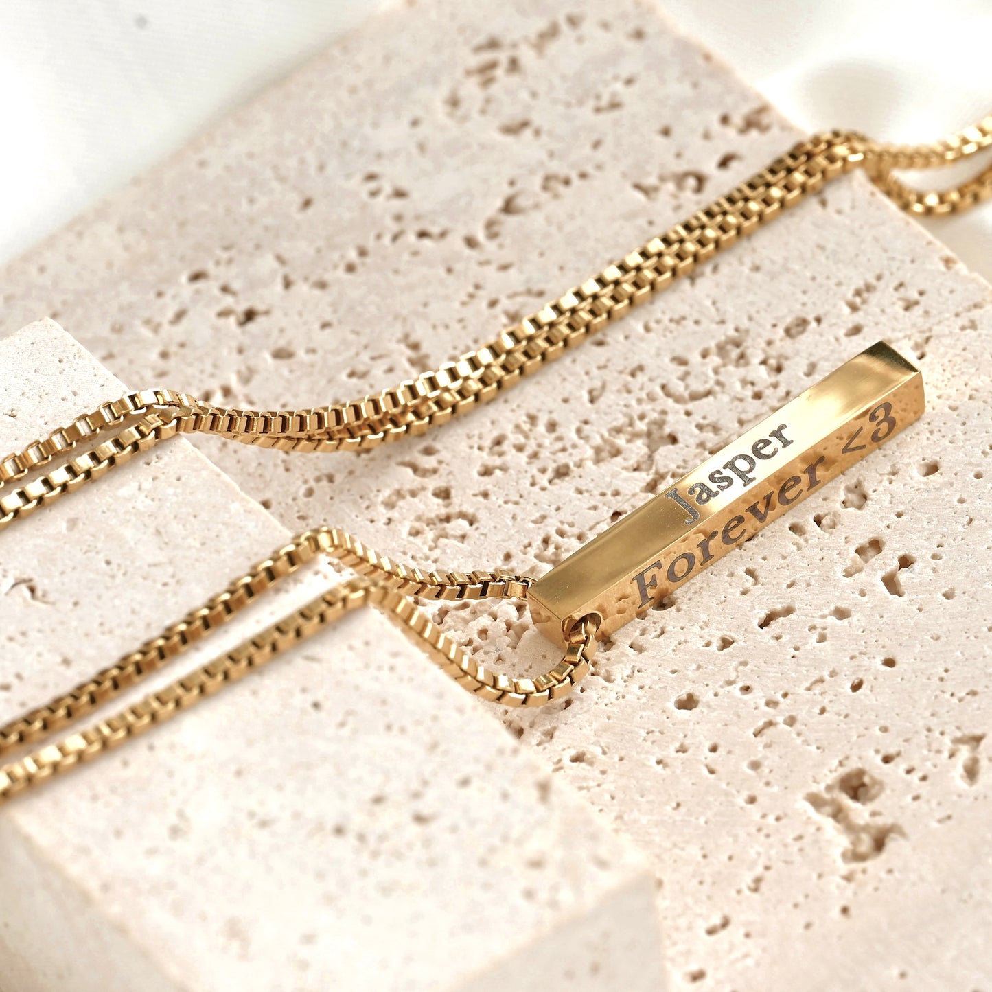 Gold necklace with a bar pendant on a textured beige surface