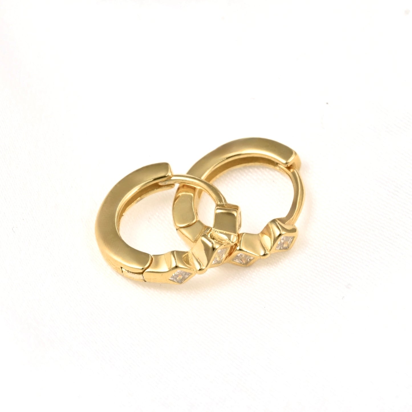 A pair of gold huggie hoop earrings with small clear crystal accents, displayed on a clean white background.