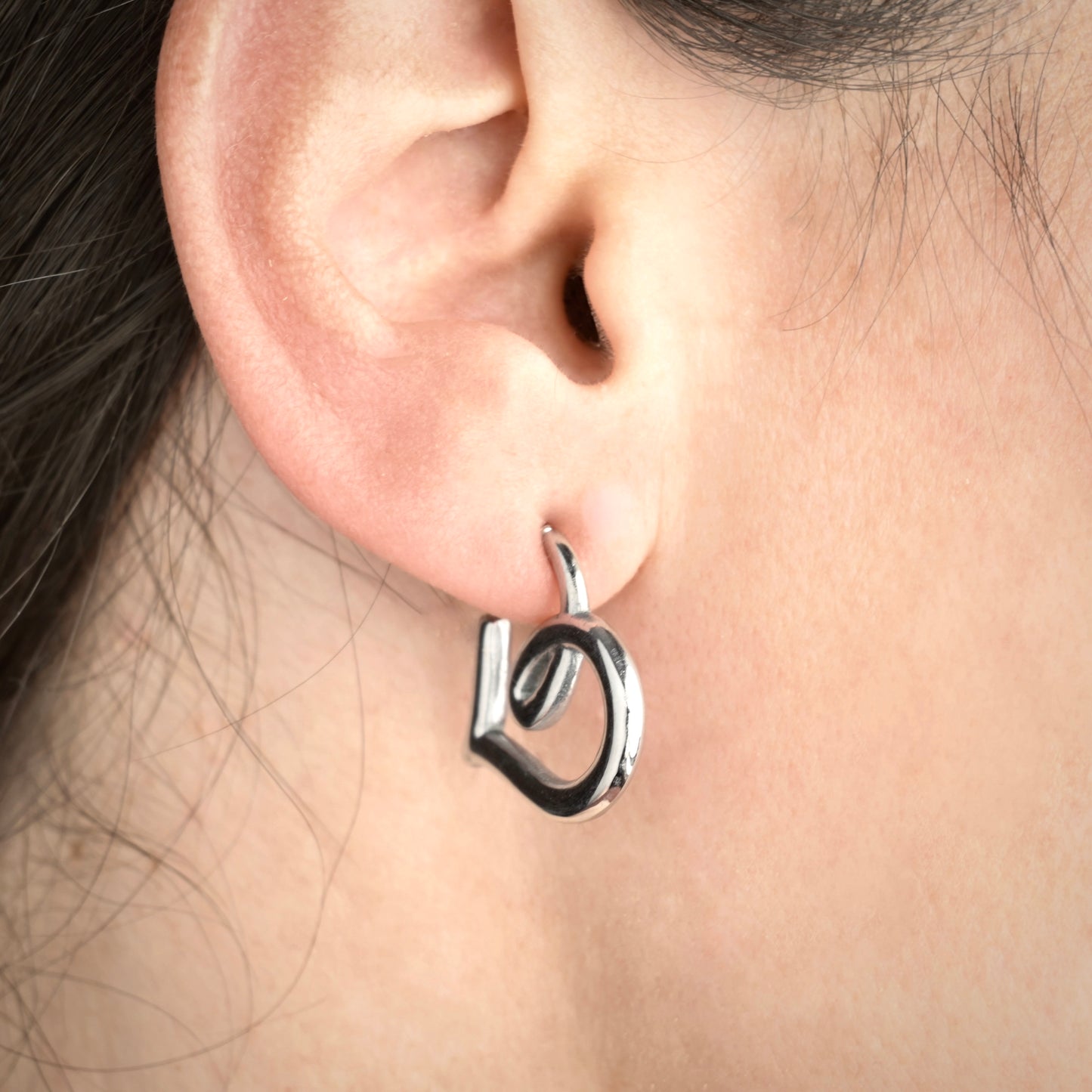 Close-up of a person wearing a silver heart hoop earring.