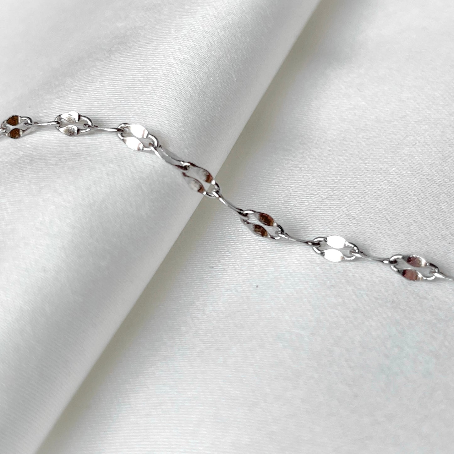 Silver-toned chain bracelet on a white fabric background