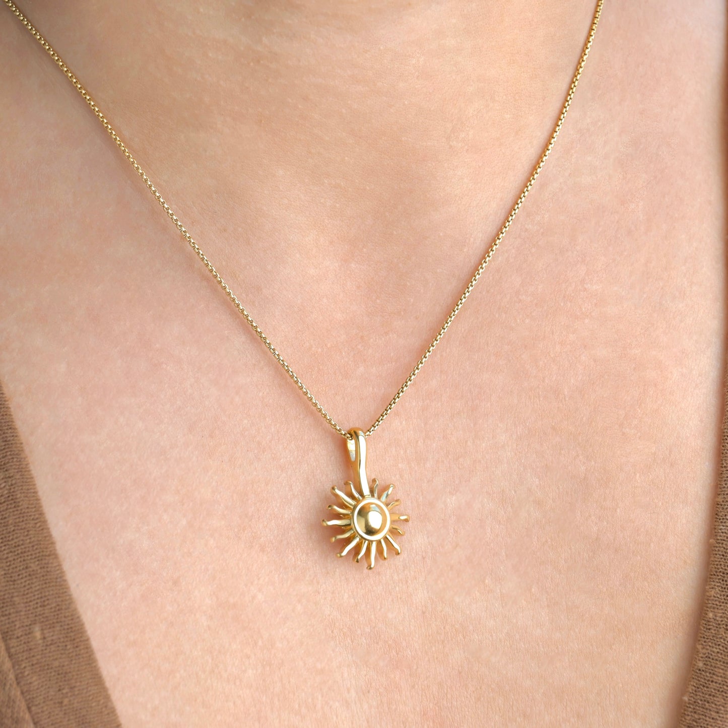 Gold necklace with a sun pendant on a person's neck
