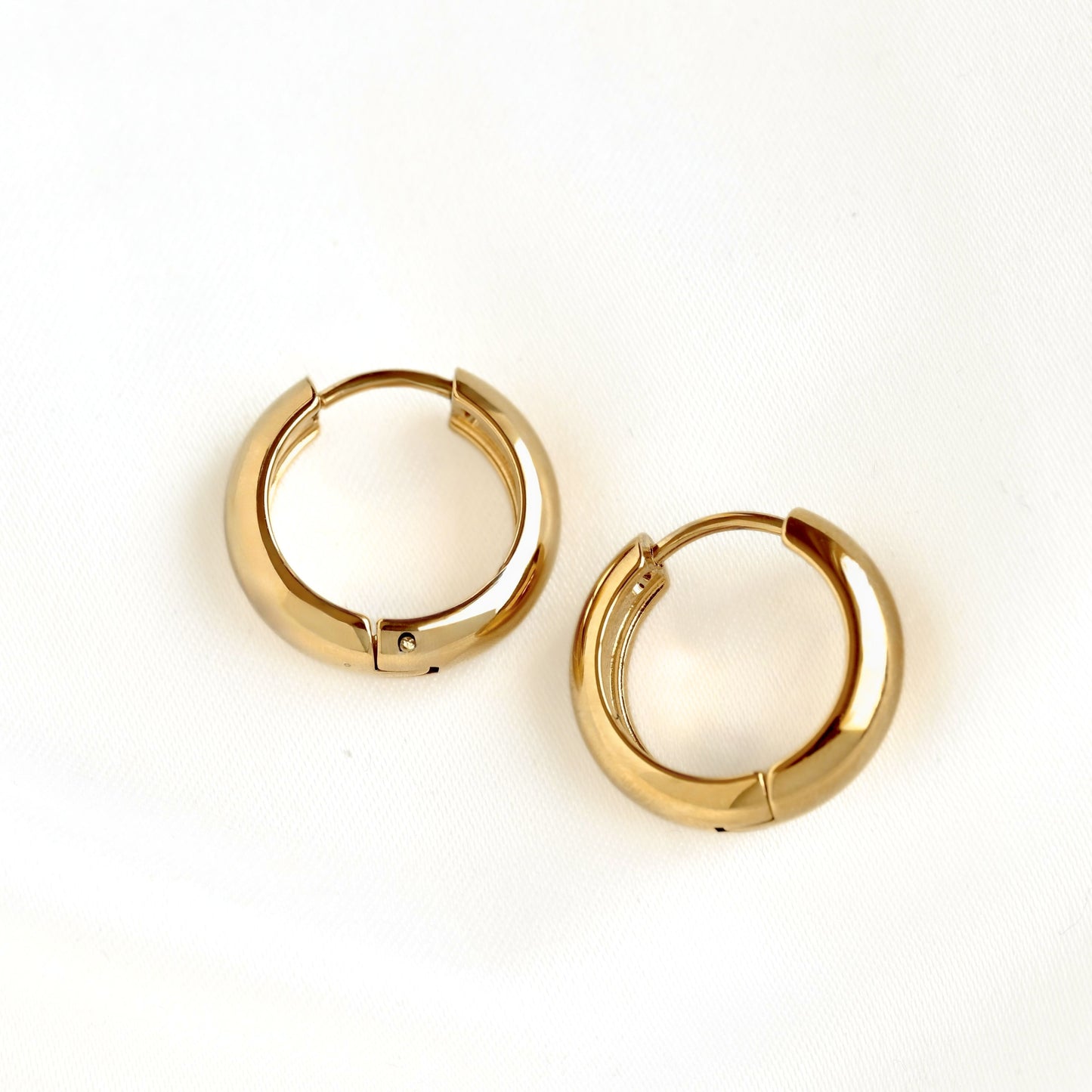 A pair of polished 17 mm gold huggie hoop earrings on a clean white textured background.
