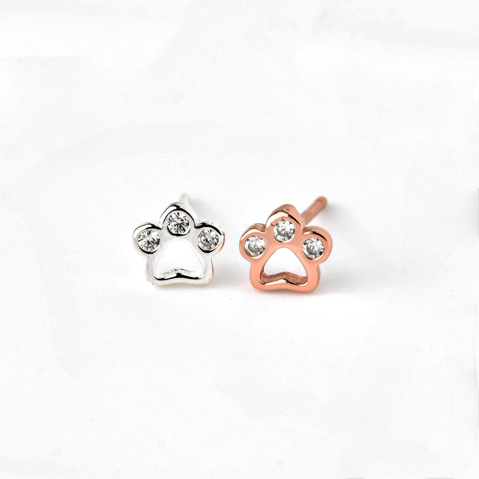 Paw-shaped earrings in silver and rose gold with three CZ stones on a white background