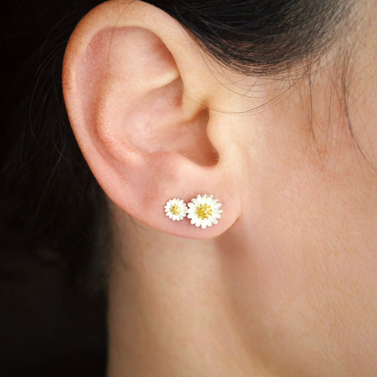 Close-up of an ear wearing white daisy earrings with a blurred background