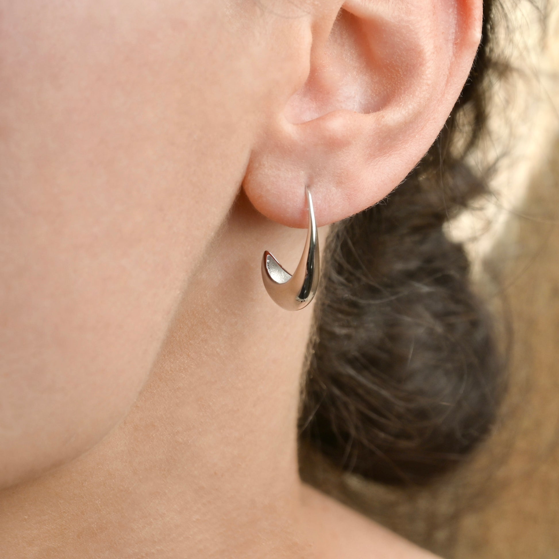 Silver drop earring worn by a person with blurred background