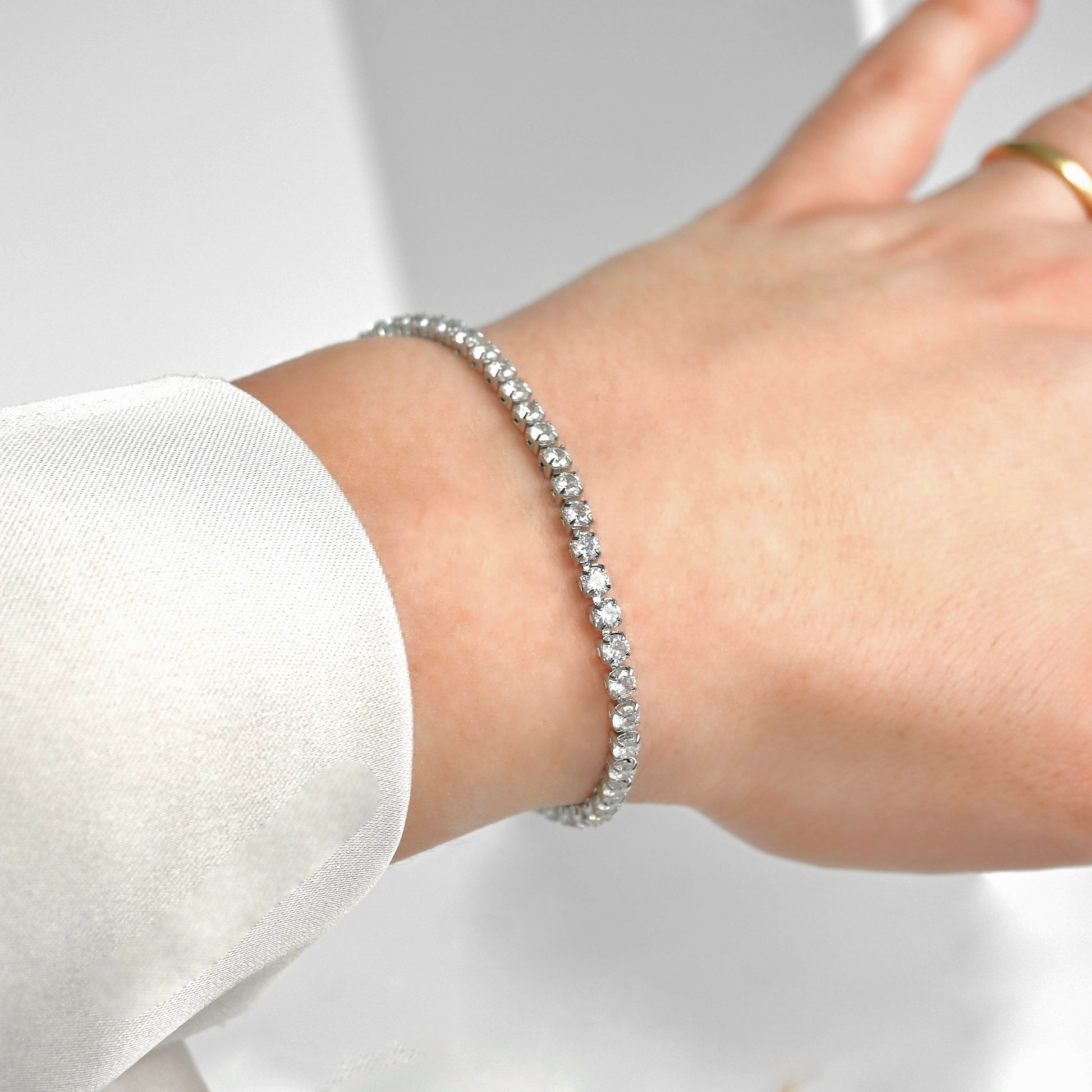 Silver tennis chain bracelet on a wrist with a blurred background