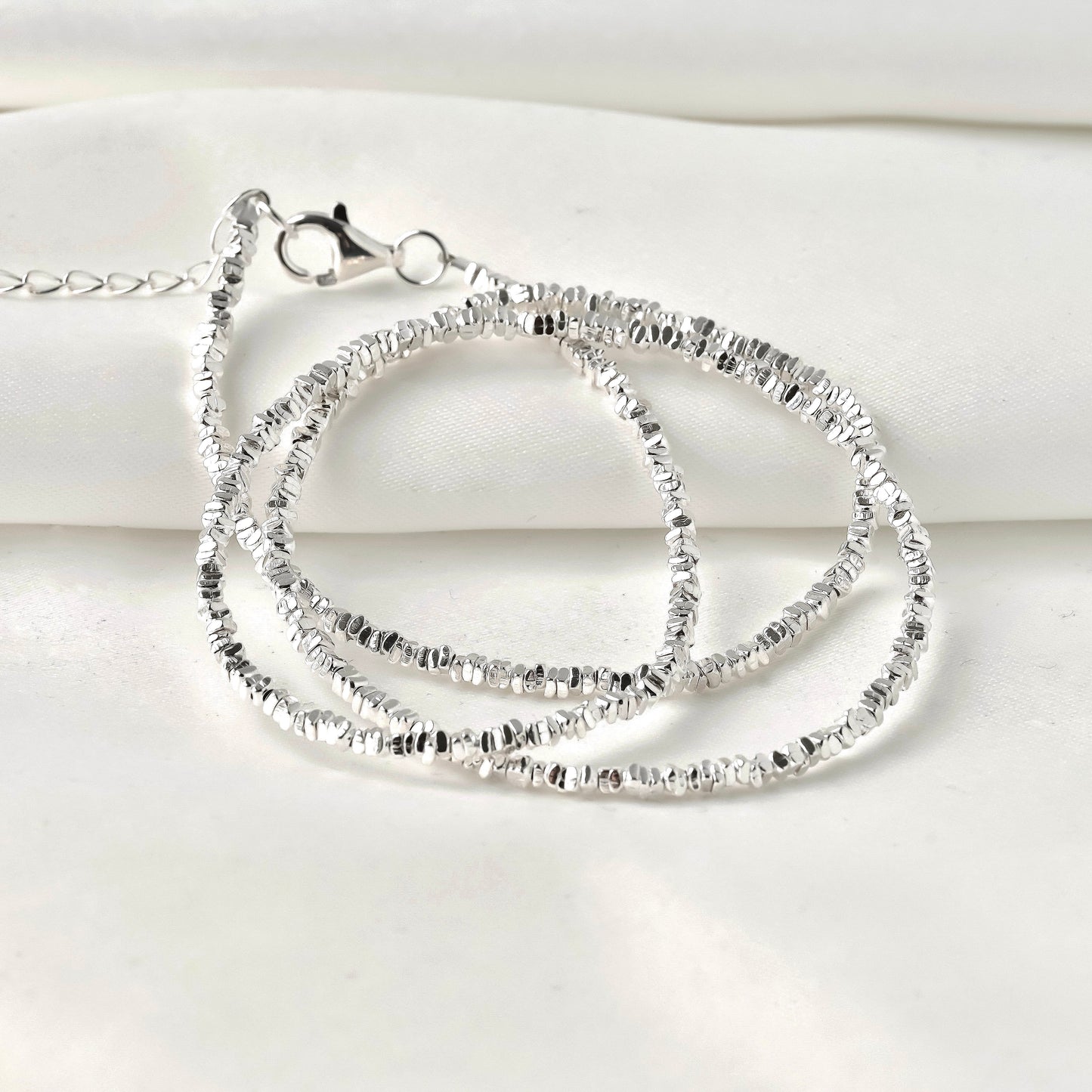 Silver necklace with clear stones coiled on a white fabric  background