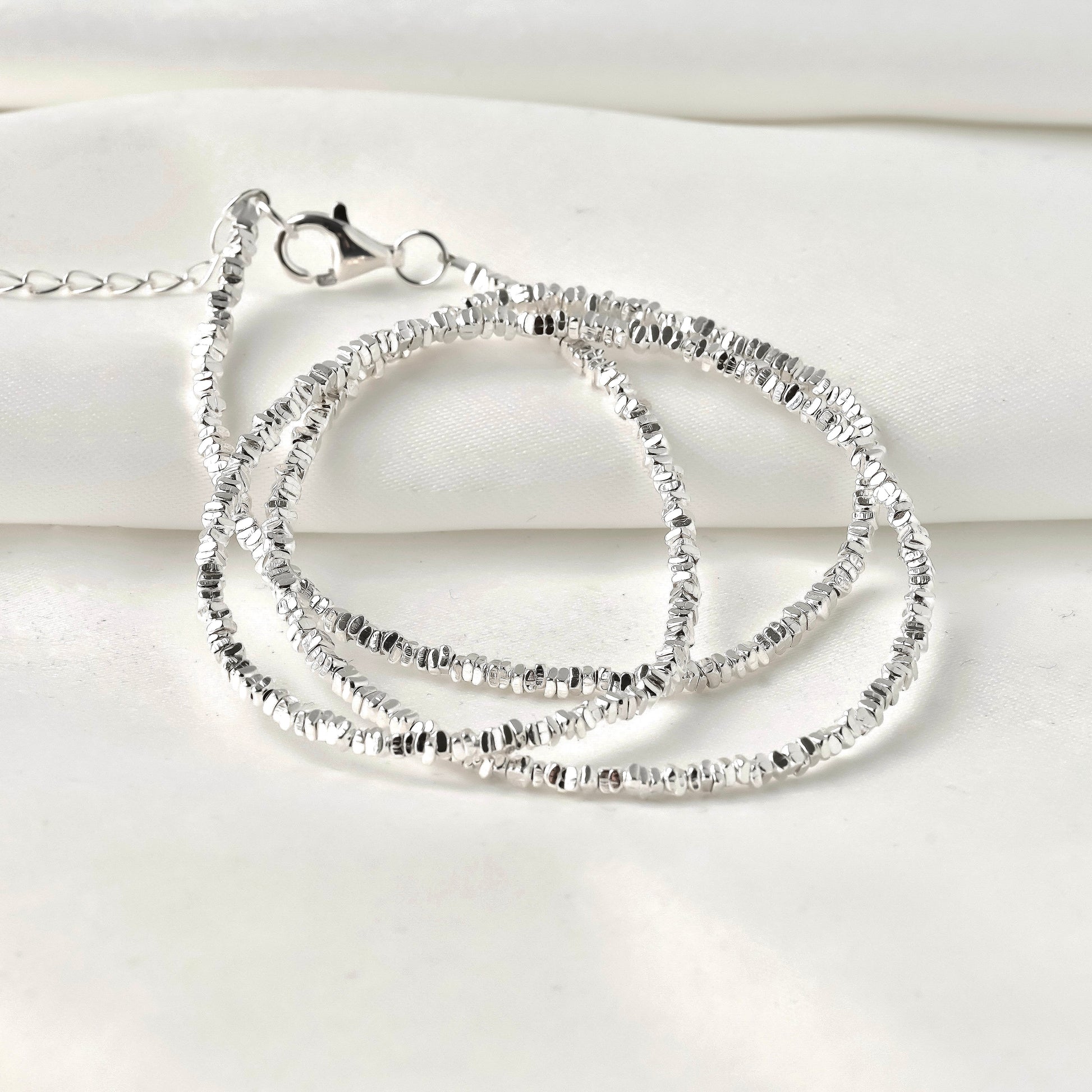 Silver necklace with clear stones coiled on a white fabric  background